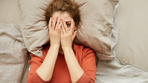 Young woman lying in her bed and hiding her face behind her hands.